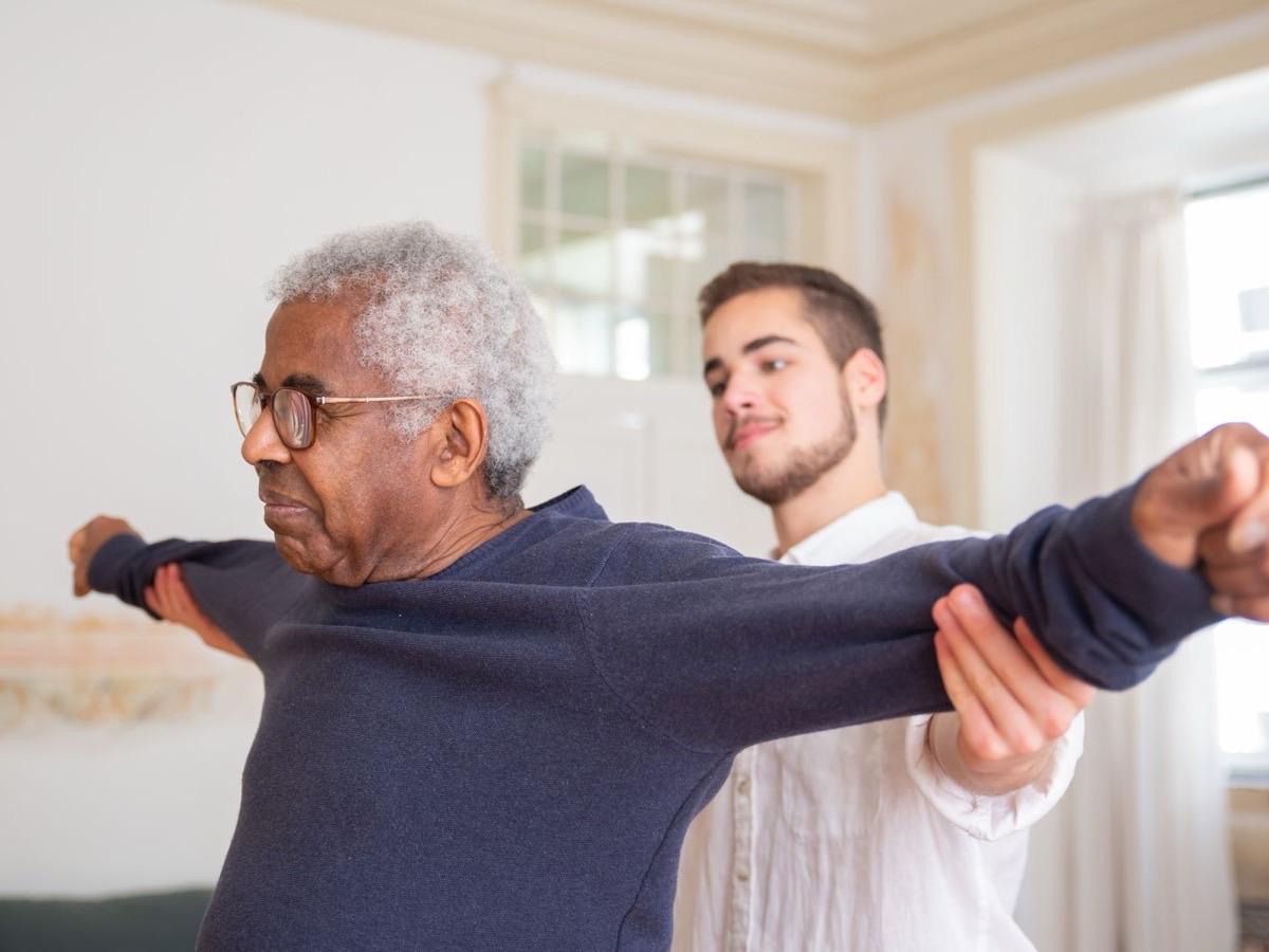 Therapist gently supporting an older man's outstretched arms during a stretching exercise