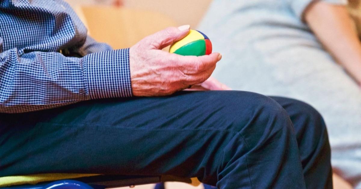 Older adult's hand squeezing a small therapy ball to exercise stiff finger joints