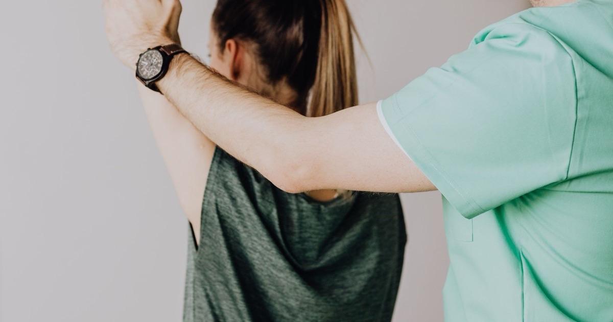 Therapist guiding a patient's raised arm through a gentle range-of-motion exercise