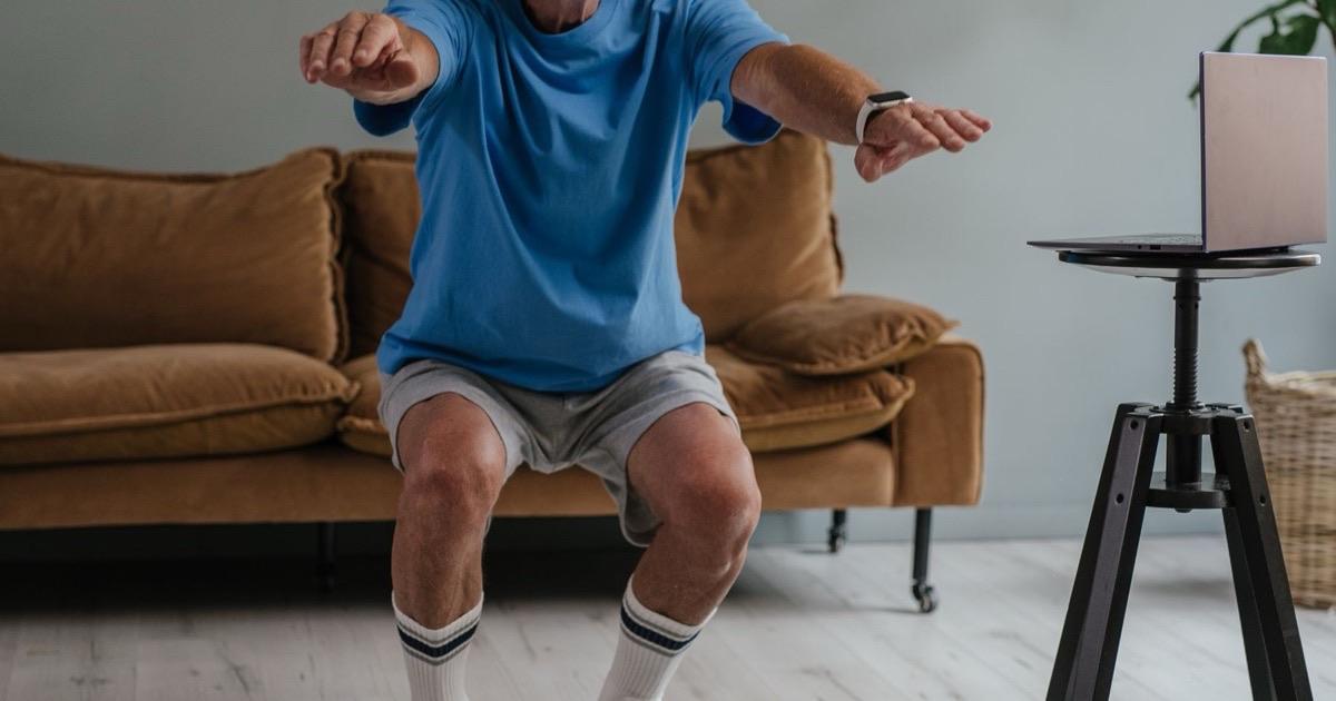 Older man performing a careful squat in his living room to strengthen his knees