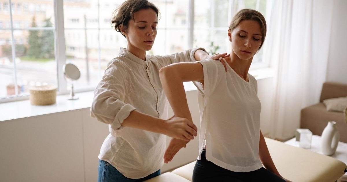 Therapist gently stretching a seated patient's shoulder and arm during a manual therapy session