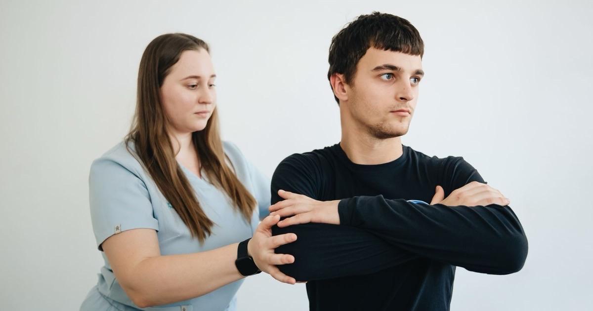 Therapist supporting a man's arm as he pulls it across his chest in a shoulder stretch