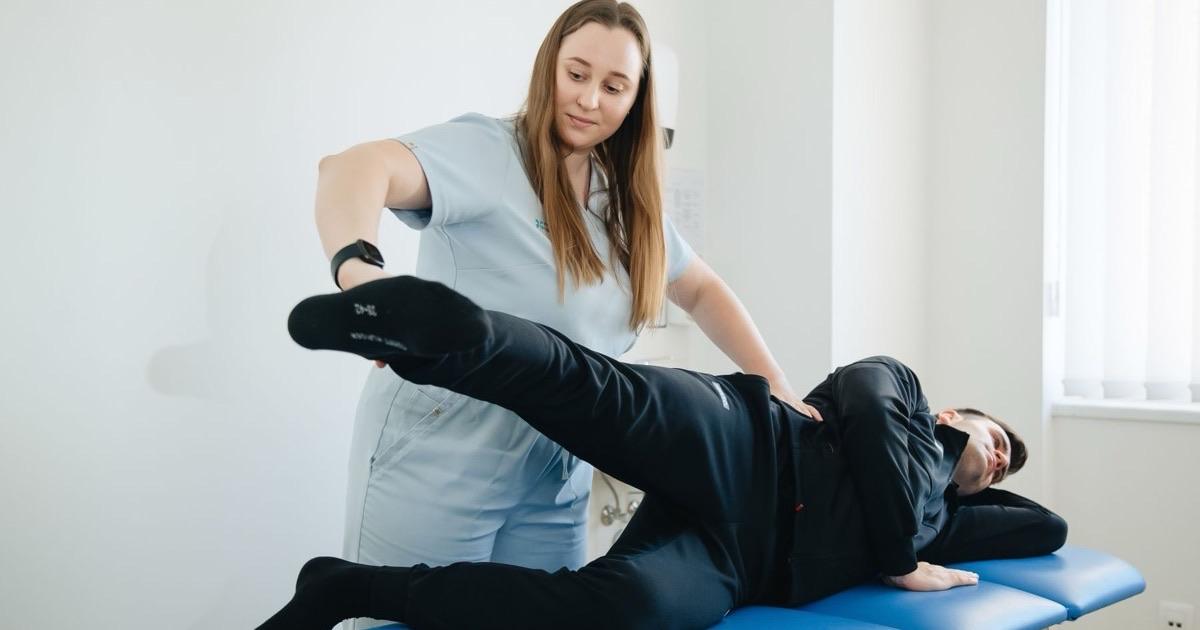 Physical therapist guiding a patient's leg through a controlled knee exercise on a treatment table