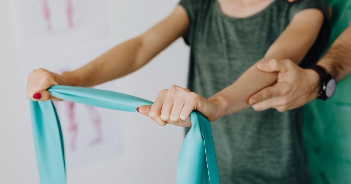 Patient stretching a resistance band with both arms while a therapist guides the exercise
